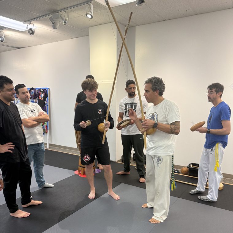 A capoeira instructor and students holding berimbaus and percussion instruments during a class.